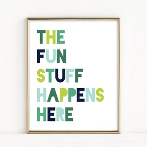 May include: A framed print with the text "THE FUN STUFF HAPPENS HERE" in a colourful, modern font. The letters are in shades of green, blue, and navy.