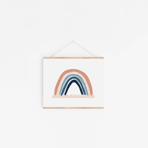 May include: A framed print of a rainbow with a peach, blue, and white color scheme. The rainbow is drawn in a simple, modern style with a white cloud underneath.