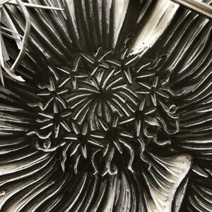 May include: A close-up of a black and white ceramic plate with a raised design of stylized flowers. The plate has a textured surface and a radial pattern.