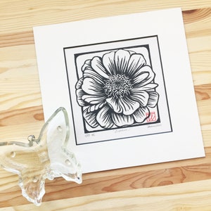 May include: Black and white woodblock print of a single Zinnia flower. The print is titled "Zinnia" and is numbered 1/15. The artist's signature and the year 2020 are in red ink in the bottom right corner.