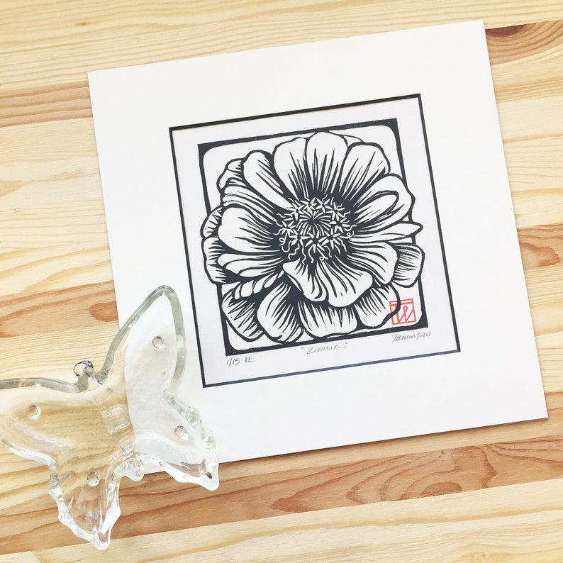 May include: Black and white woodblock print of a single Zinnia flower. The print is titled "Zinnia" and is numbered 1/15. The artist's signature and the year 2020 are in red ink in the bottom right corner.