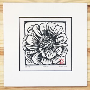 May include: Black and white linocut print of a single flower with the title "Zinnia" and the number "1/15" in the bottom left corner. The print is signed and dated "Tania 2020" in the bottom right corner.