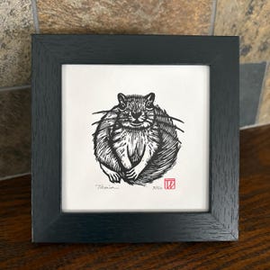 May include: Black framed print of a squirrel linocut. The print is signed "Tania" with the edition number 3/50 and a red stamp. The squirrel is depicted in black and white with detailed linework, set against a white background.