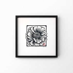 May include: Black and white woodblock print of a single flower with a red stamp in the bottom right corner. The print is framed in a black frame.