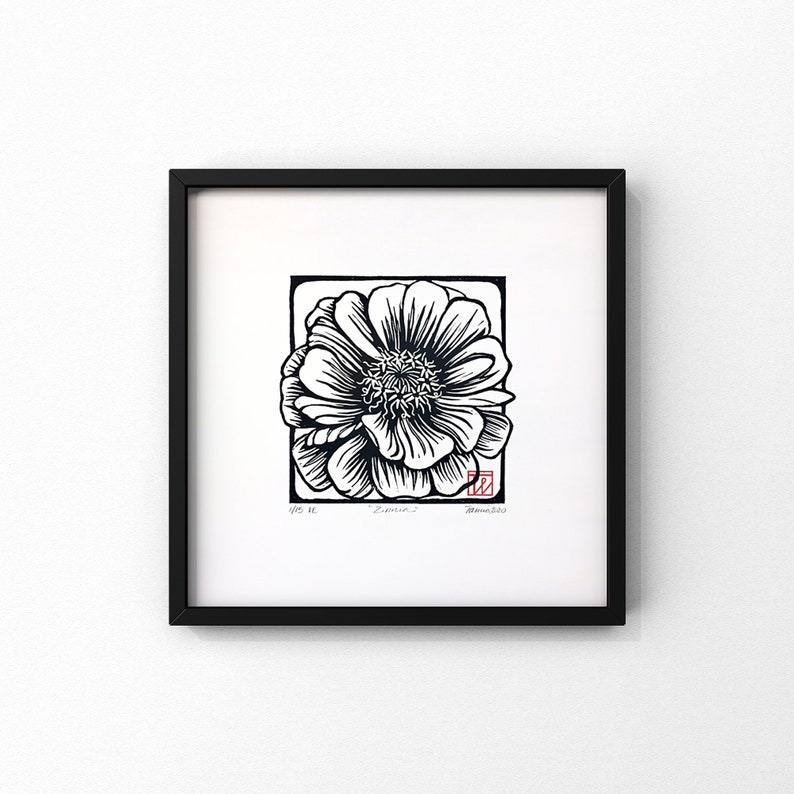 May include: Black and white woodblock print of a single flower with a red stamp in the bottom right corner. The print is framed in a black frame.