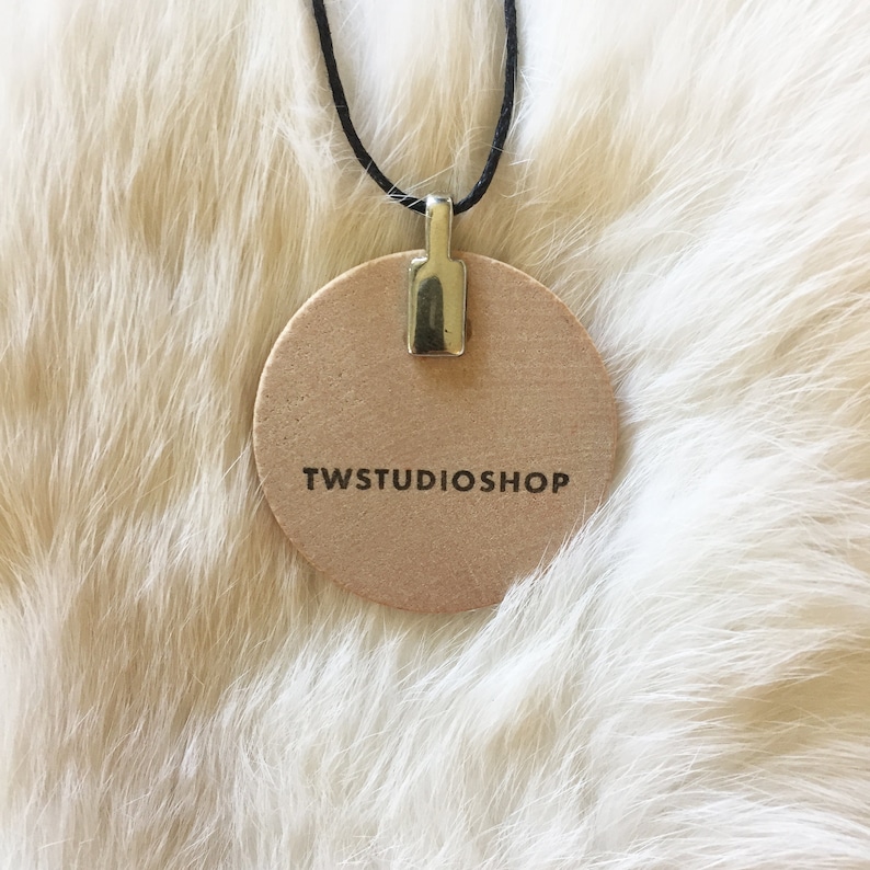 May include: A round, brown, leather tag with a silver metal loop and the text "TWSTUDIOSHOP" printed in black.