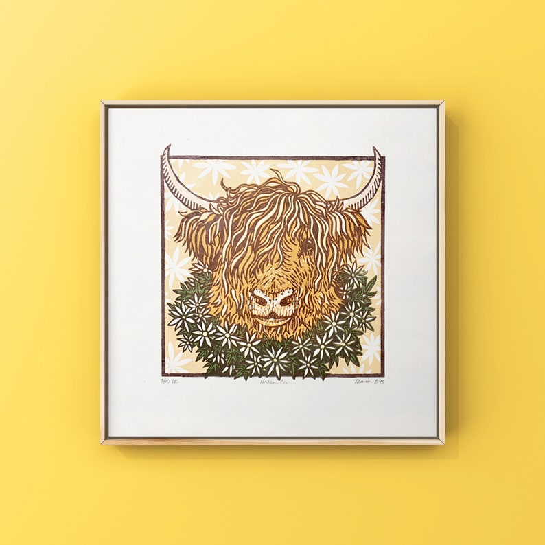 Puede incluir: Una impresi&oacute;n en madera de una vaca de las Tierras Altas con una corona de flores alrededor del cuello. La impresi&oacute;n es en tonos de marr&oacute;n, amarillo y verde, y est&aacute; enmarcada en un marco de madera claro.