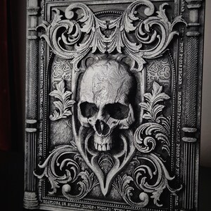 May include: A black and white 3D printed book cover with an ornate design featuring a skull in the center. The cover has a gothic style with intricate details and a textured surface. The text on the cover reads "DOMINUS NOTA TOBS MALA, OFTIMA SUMOL JUSTUS BT PECCATOR", "UBITO BRA", "HOMO UNTUS LIBIU TIMRO VERITAS VOS LIBERABIT", "TANTAST", "CORTALIUM", "CABSAR", "NTT NON POSSE FECARE", "HABEMUS PAPARC NON POSSE", "NON PH", "SAR BST", "STAL", "FIS PATRIET PILIO ET VILLAB ET SPIRITOS SANCTI AUT".