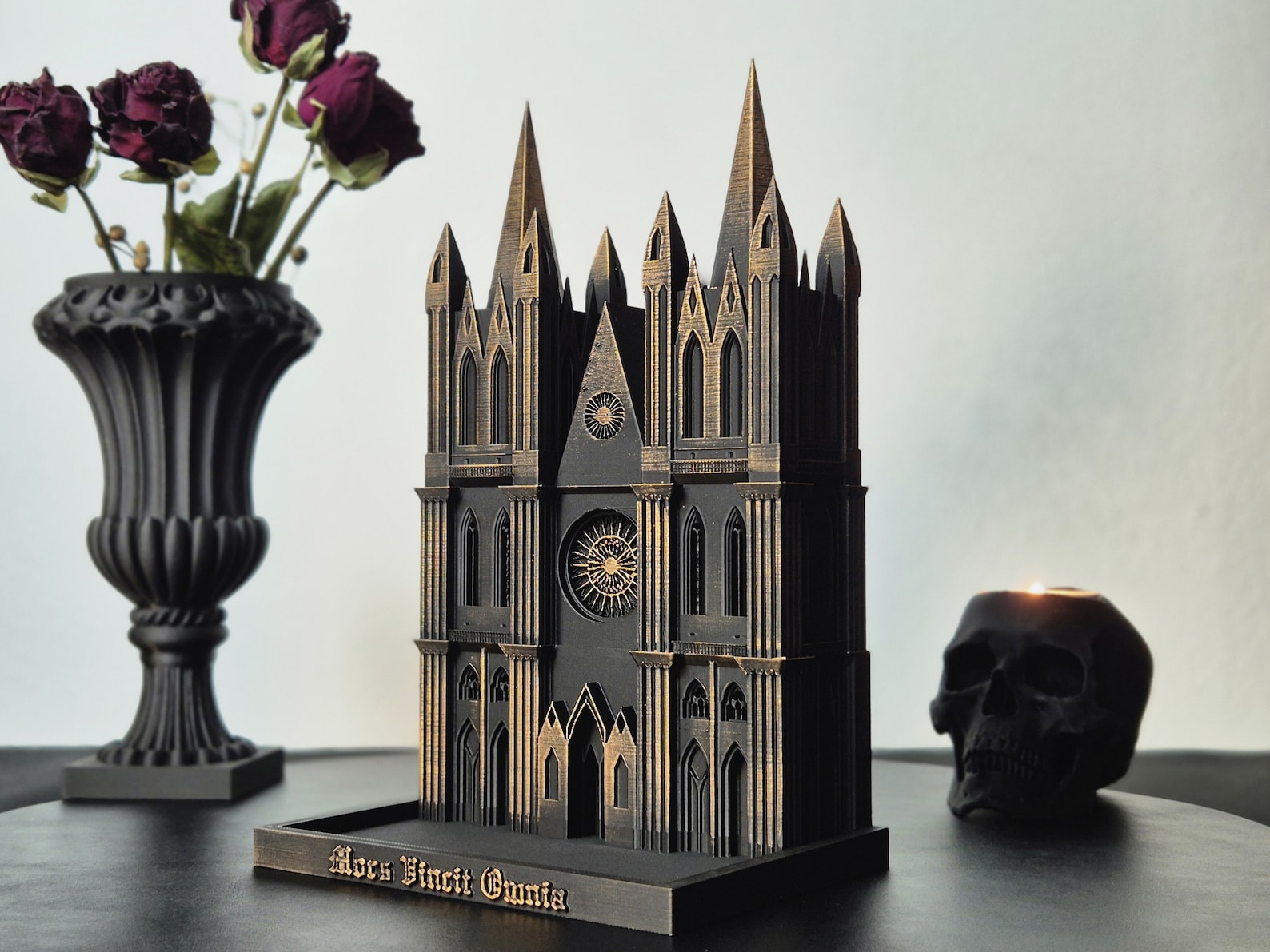 Black and gold 3D-printed Gothic cathedral tray surrounded by a black vase with dried roses and a black skull candle on a dark tabletop