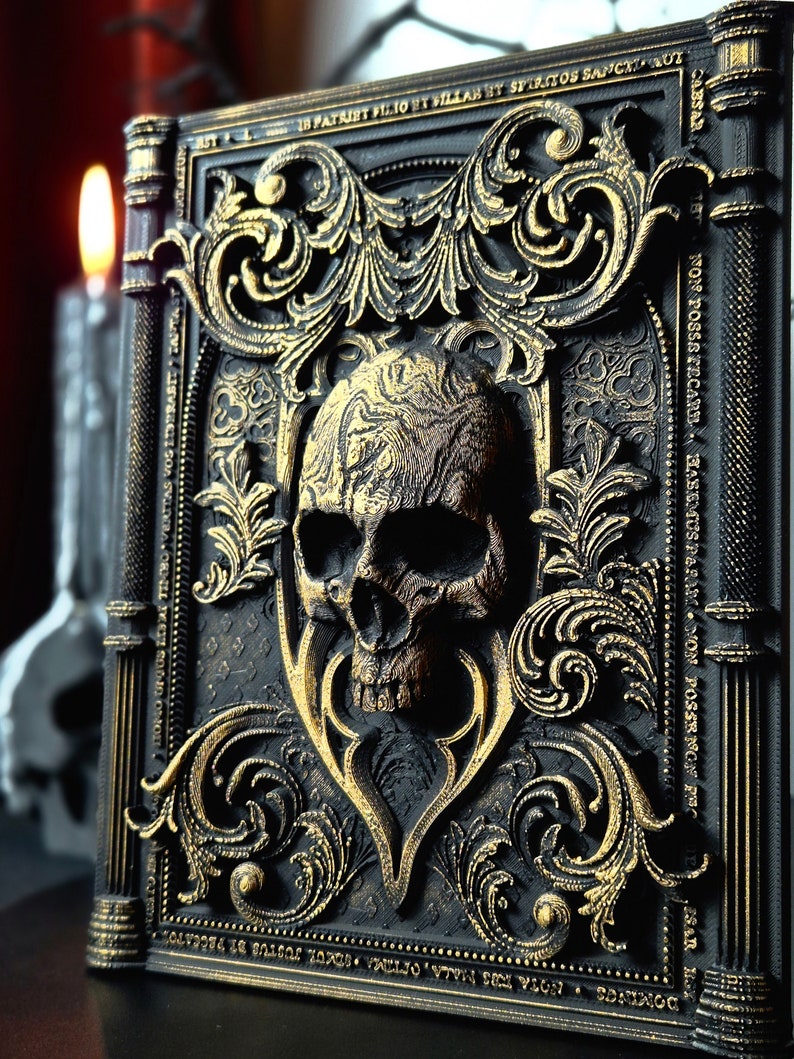 May include: A black and gold book cover with an ornate design. The cover features a skull with gold accents and the text "DOMINGS ROTA TUS MALA, OFIIMA TIMA SOKOL JUSTUS BЕ РАССАТОТ ONOUS LESAI TINHO VERITAS VOS ITSPRASIT ORTALCIUM PATAIRT FILIOT VILLAH HT SPIRITOS SANCXTRACT CABSAR NON POSSSTECARE HASEMUS PARAM NON POSSR NON PRO ESAR".