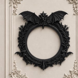 Op de afbeelding: Een zwarte, gotische, cirkelvormige lijst met een vleermuis en sierlijke details. De lijst is gemonteerd op een crèmekleurige muur met decoratieve lijstwerk. De vleermuis, met uitgespreide vleugels, staat bovenaan.