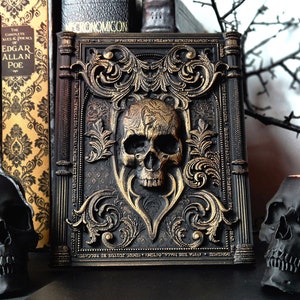 May include: A black book with gold accents and a skull design on the cover. The book is titled "Necronomicon" and has a gothic style. The book is surrounded by black skulls and candles.