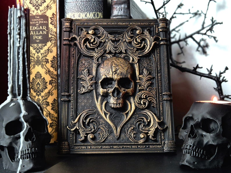 May include: A black book with gold accents and a skull design on the cover. The book is titled "Necronomicon" and has a gothic style. The book is surrounded by black skulls and candles.