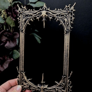Puede incluir: Marco de fotos gótico ornamentado, negro y dorado. El marco presenta detalles intrincados y puntiagudos y un diseño de arco apuntado. El marco está vacío, con un fondo oscuro.