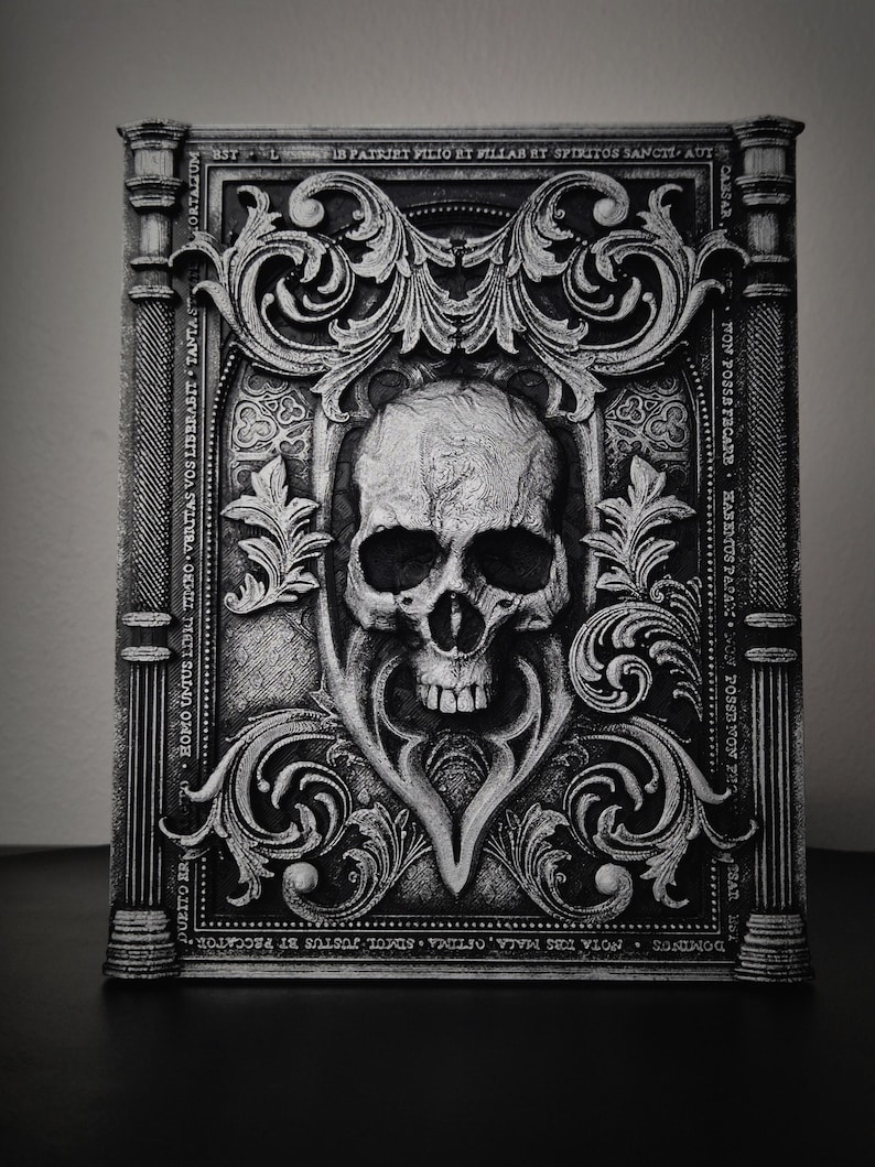 May include: A black and white decorative skull with ornate scrollwork and text around it. The text reads "DUBITO ER HOMO UNIUS LIBRI TIMBO VERITAS VOS LIBERABIT TANTAST CORTALIUM, BSTLIB PATRIET PILIO ET VILLAB ET SPIRITOS SANCIT AUT CABSAR FON POSSAFECARE HASEMUS PAPAX WON POSSENON PHO SAT H DOMINGS NOTA TBS MALA, OFTIMA SIMUL JUSTUS BT PECCATOR".