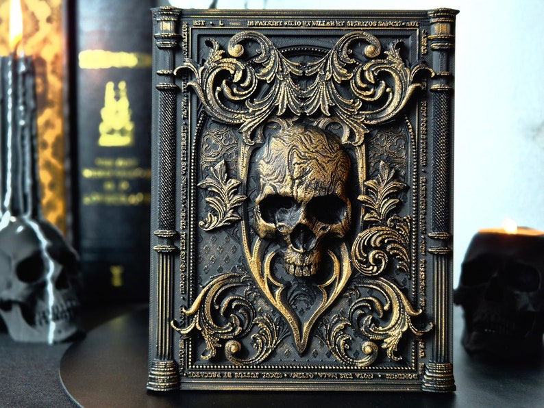 May include: A black book with a gold skull and ornate design. The book is decorated with gold filigree and has a skull on the front cover. The book is closed and standing upright on a table.