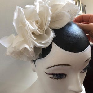 May include: A white fabric flower headpiece with multiple layers of petals. The flower is pinned to a black and white mannequin head.