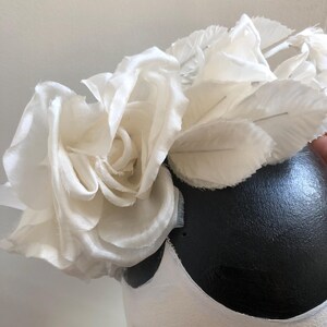 May include: A white fabric flower crown with a large white rose in the center. The crown is made of several layers of fabric and has a delicate, feminine look.