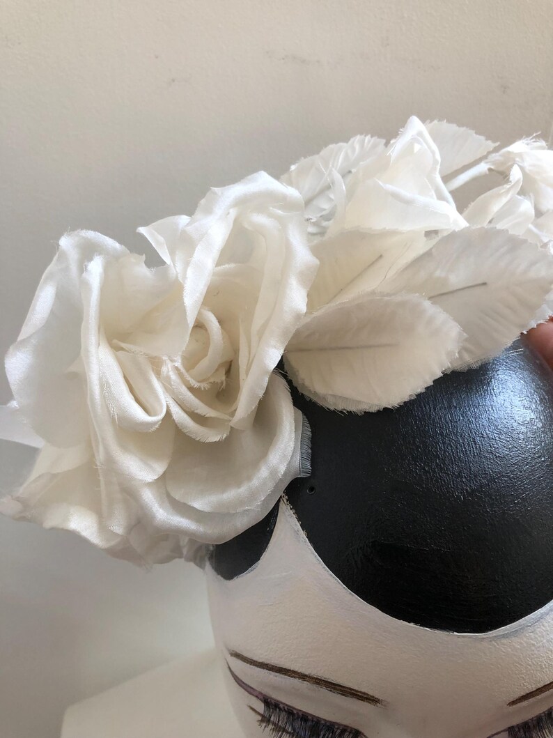 May include: A white fabric flower crown with a large white rose in the center. The crown is made of several layers of fabric and has a delicate, feminine look.