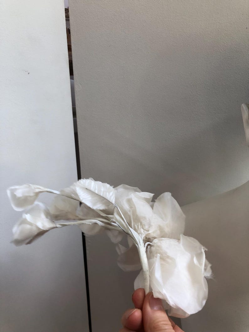 May include: A white silk flower with a delicate, layered design. The flower is made of multiple petals and has a long, thin stem.