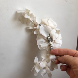 May include: A white dried flower arrangement with a silver and white decorative piece in the center.