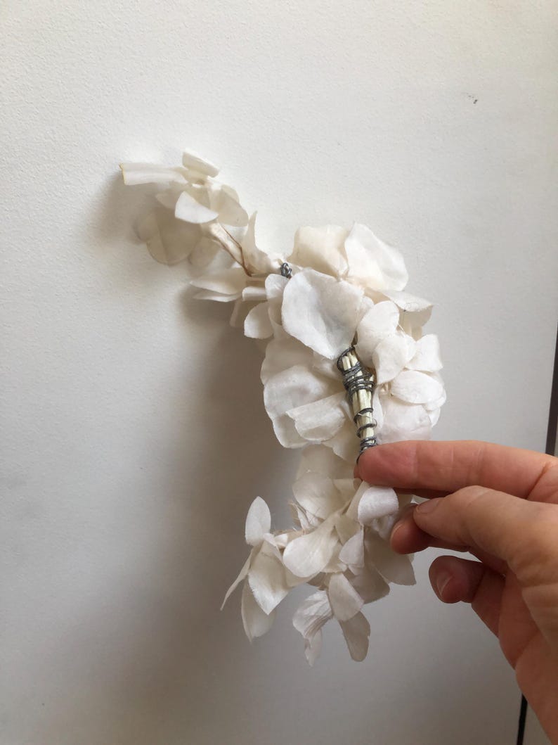 May include: A white dried flower arrangement with a silver and white decorative piece in the center.