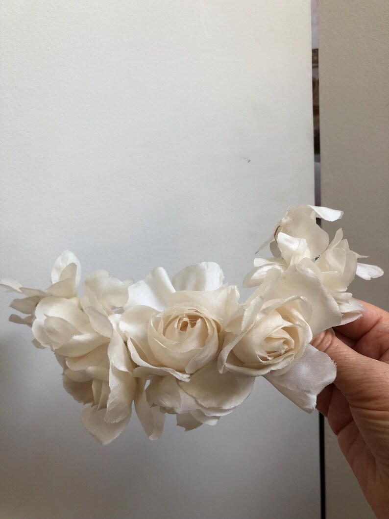 May include: A white flower crown made of silk roses. The crown is made of several roses, each with a different number of petals. The roses are arranged in a circle, with the petals overlapping.