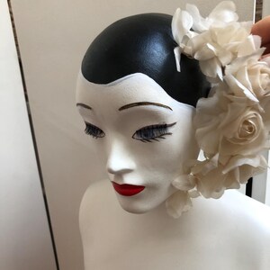 May include: A white mannequin head with black hair and red lips, wearing a white flower crown.