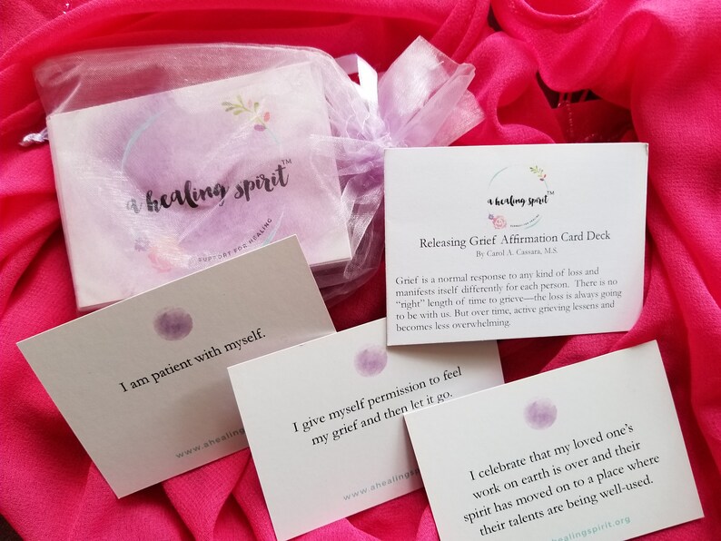 May include: Affirmation cards for grief release, featuring the text "a healing spirit". The cards include affirmations such as "I am patient with myself" and "I give myself permission to feel my grief." The cards are displayed on a pink fabric background.
