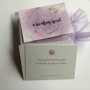 May include: A stack of cards with the text "a healing spirit" and "Support for Healing" on the top card. The card below reads "I am patient with my grief. It will take as long as it takes." The cards are wrapped in a lavender organza bag.
