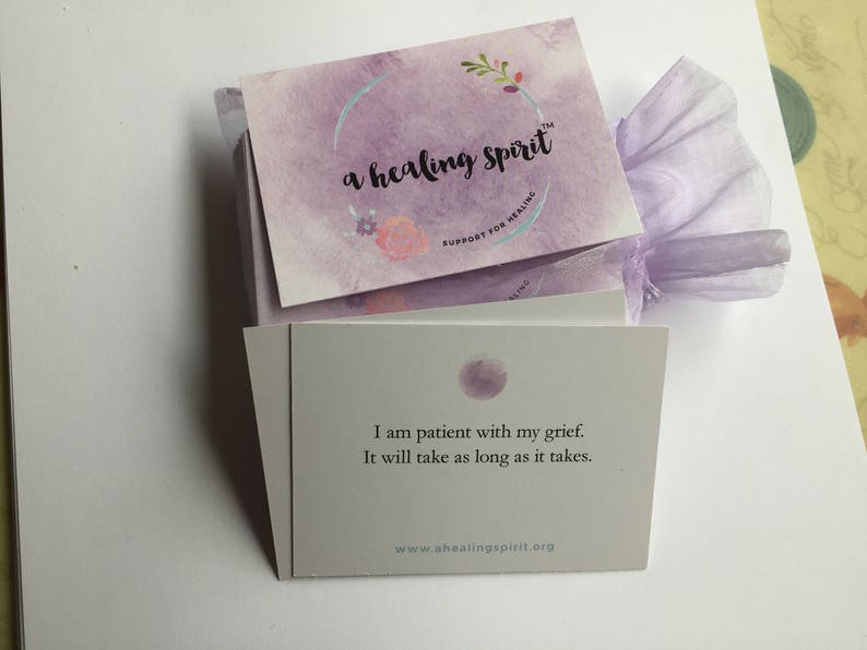 May include: A stack of cards with the text "a healing spirit" and "Support for Healing" on the top card. The card below reads "I am patient with my grief. It will take as long as it takes." The cards are wrapped in a lavender organza bag.
