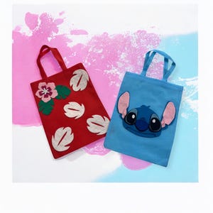 May include: Two tote bags. One is red with a flower and leaf design. The other is blue with a cartoon character face. Both have matching handles. The background is a mix of pink and blue.