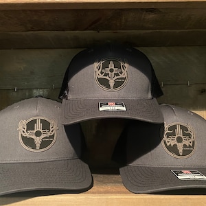 May include: Three gray and black mesh trucker hats with a brown embroidered logo of a deer skull with antlers and a sun symbol inside a circle. The logo also includes the text "Classic Co."