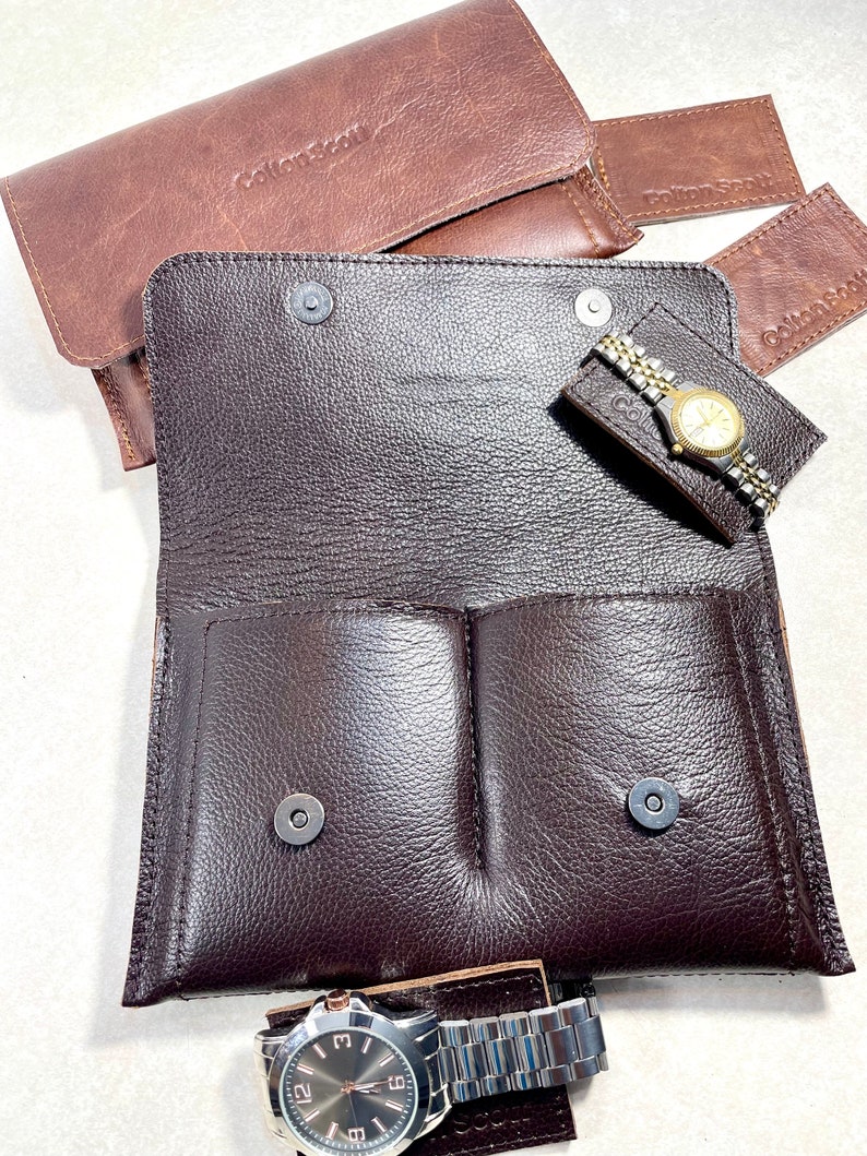 K&ouml;nnte beinhalten: Ein braunes Lederuhrenetui mit zwei F&auml;chern und einem Druckknopfverschluss. Das Etui tr&auml;gt ein Etikett mit der Aufschrift "Collections by".