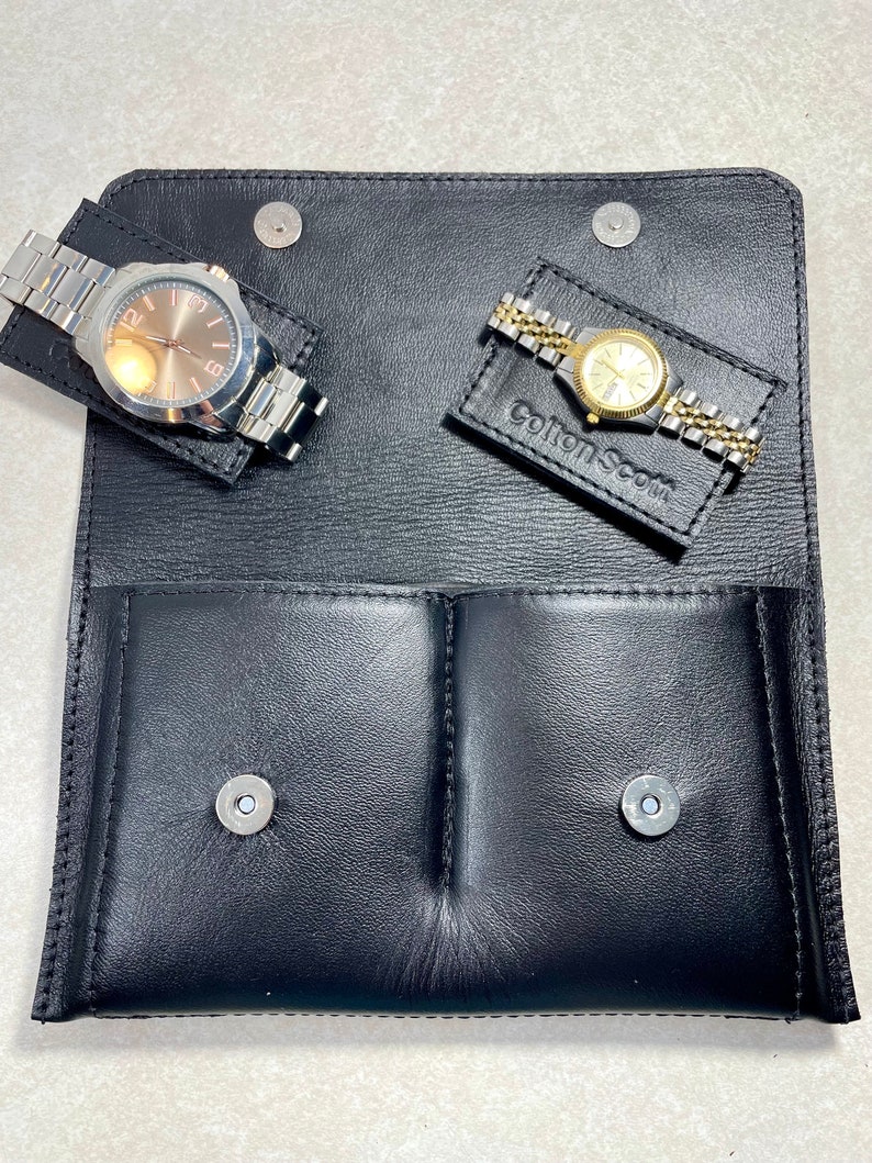 K&ouml;nnte beinhalten: Schwarze Lederuhr-Etui mit zwei F&auml;chern zur Aufbewahrung von Uhren. Das Etui hat zwei silberne Druckkn&ouml;pfe und der Text "Cotton & Scott" ist auf der Vorderseite gepr&auml;gt.