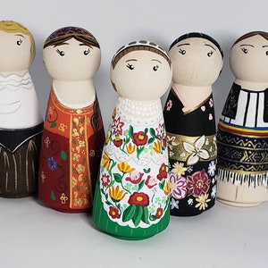 Puede incluir: Cinco muñecas de madera con clavijas vestidas con trajes tradicionales folclóricos. Las muñecas están pintadas en colores brillantes con detalles intrincados. Los trajes presentan patrones florales, diseños geométricos y bordados.