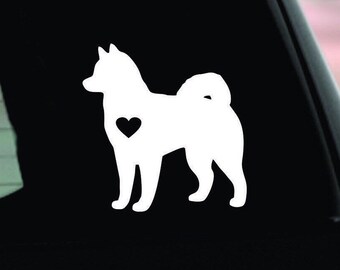 May include: A white vinyl decal of a dog silhouette with a heart-shaped cutout on its side. The dog has a fluffy tail and is facing left. The decal is likely for a car window or similar surface.