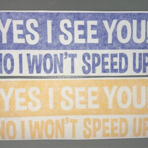 May include: Two rectangular bumper stickers with white text on colored backgrounds. The top sticker is blue with white text reading YES I SEE YOU! NO I WON'T SPEED UP! The bottom sticker is yellow with white text reading YES I SEE YOU! NO I WON'T SPEED UP!
