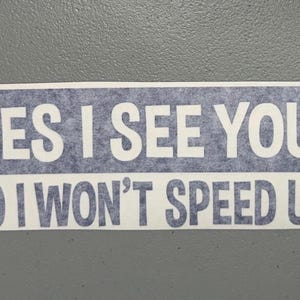 May include: A rectangular bumper sticker with a blue textured background and white text that reads YES I SEE YOU! NO I WON'T SPEED UP! The sticker features bold, block-style lettering arranged in two lines against the blue backdrop.
