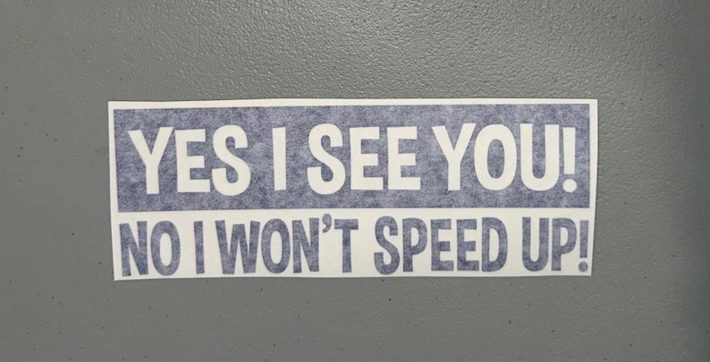 May include: A rectangular bumper sticker with a blue textured background and white text that reads YES I SEE YOU! NO I WON'T SPEED UP! The sticker features bold, block-style lettering arranged in two lines against the blue backdrop.