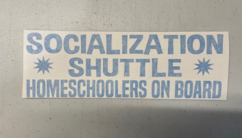 May include: A rectangular white vinyl sticker featuring light blue text that reads SOCIALIZATION SHUTTLE HOMESCHOOLERS ON BOARD. The design includes two light blue star-shaped icons positioned on either side of the word SHUTTLE.
