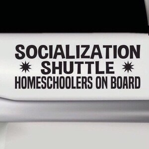 May include: A black vinyl decal applied to a white surface featuring the text SOCIALIZATION SHUTTLE with two star symbols on either side of the word SHUTTLE and the text HOMESCHOOLERS ON BOARD printed in a bold sans-serif font below.
