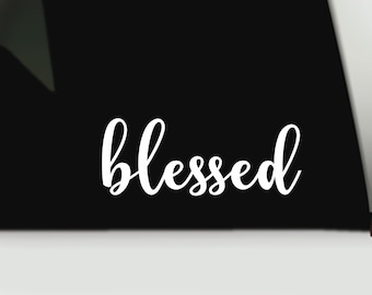 May include: A black surface featuring the word blessed written in a white, cursive, script-style font. The text is positioned horizontally across the lower portion of the black background, creating a high-contrast visual display.