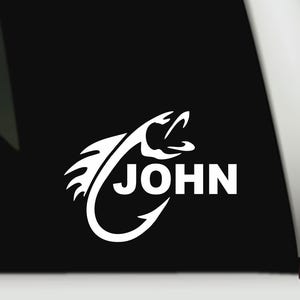 May include: White vinyl decal featuring a stylized fish hook design with the name "JOHN" in bold, capital letters. The design includes a fish head and a curved hook, suitable for fishing enthusiasts.