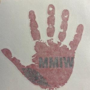 K&ouml;nnte beinhalten: Ein roter Handabdruck mit einer schwarzen Feder und dem Text "MMIW" in schwarzen Buchstaben.
