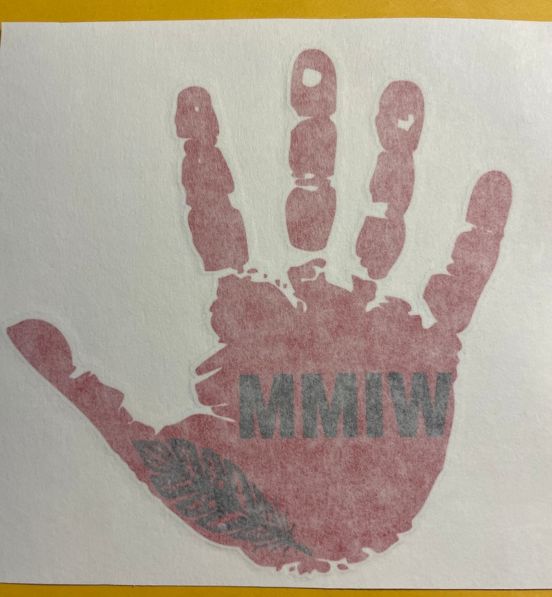 K&ouml;nnte beinhalten: Ein roter Handabdruck mit einer schwarzen Feder und dem Text "MMIW" in schwarzen Buchstaben.