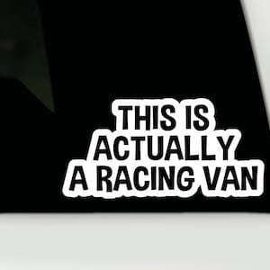 May include: A white sticker with the text "THIS IS ACTUALLY A RACING VAN" in a bold, sans-serif font. The sticker is on a black background, possibly a car window, with a white border.