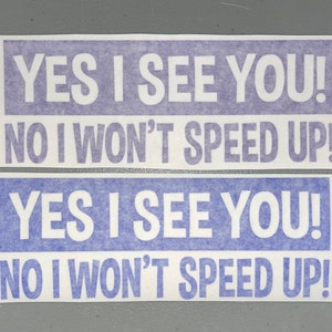 May include: Two rectangular bumper stickers featuring white text on a purple background. The text on both stickers reads: YES I SEE YOU! NO I WON'T SPEED UP! The stickers are arranged one above the other, displaying the same message clearly.