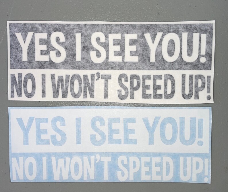 May include: Two rectangular bumper stickers with white text on a dark background and white text on a light blue background. Both stickers feature the text: YES I SEE YOU! NO I WON'T SPEED UP! The lettering is in a bold, sans-serif font style.