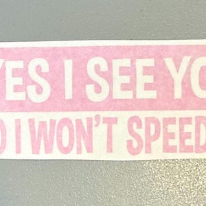 May include: A rectangular sticker with a light pink background and white text that reads YES I SEE YOU! NO I WON'T SPEED UP! The lettering is in a bold, sans-serif font, arranged in two lines with an exclamation point at the end of each.